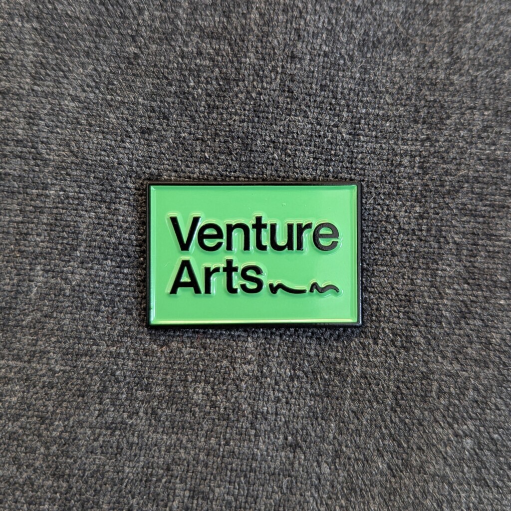 Venture Arts pin badge - Venture Arts logo in black on green background