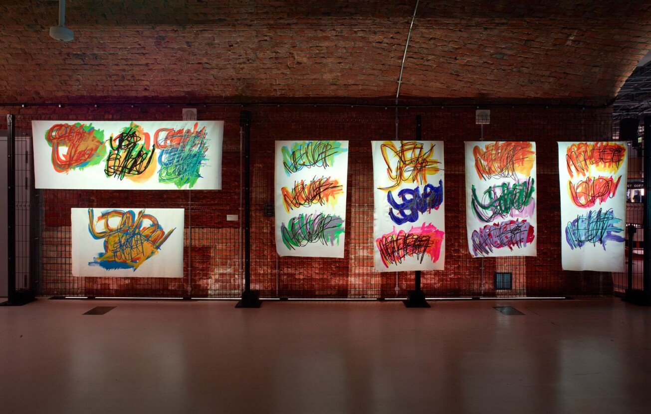 A selection of Michael Beards bold colourful work on display against a brick wall in Aviva Studios