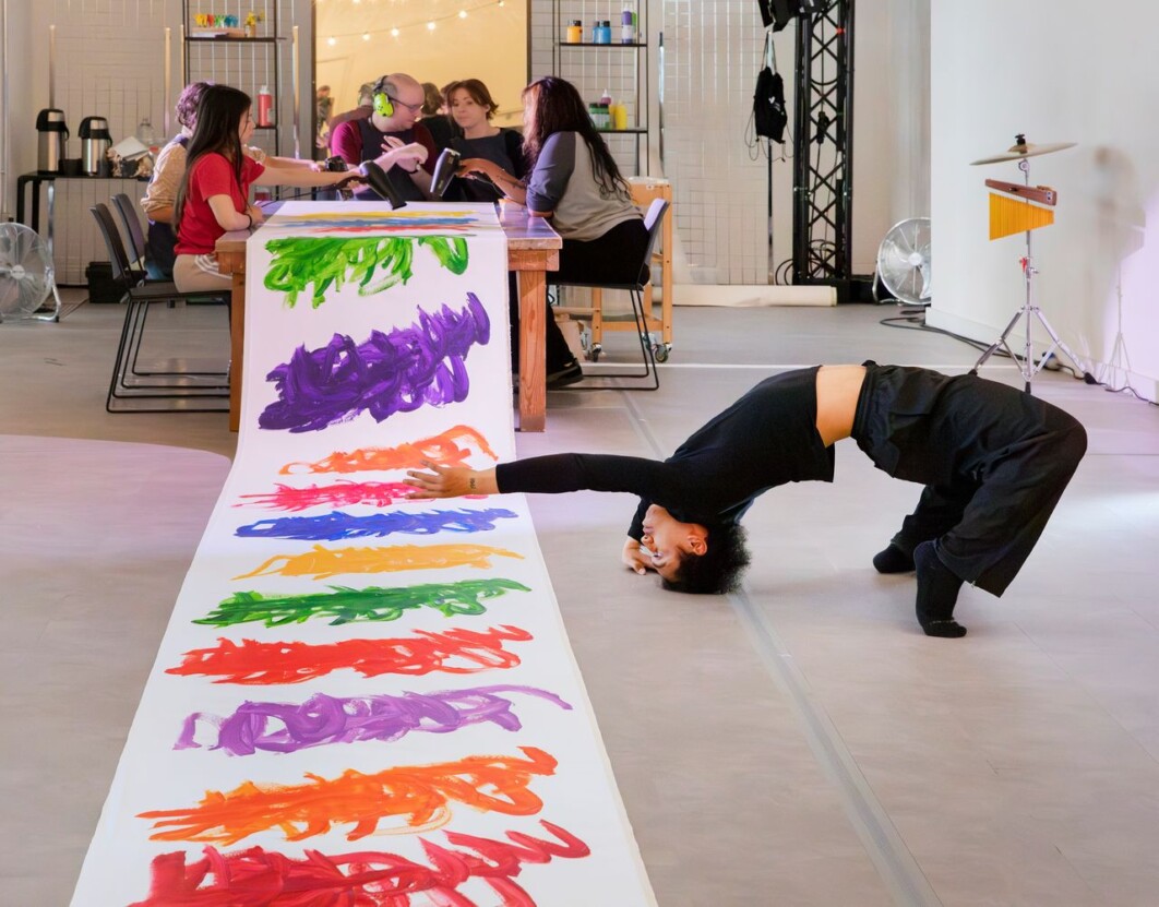 A colourful roll of Michael beard's artwork flowing from a table where he is working, with a dancer dancing alongside the work.