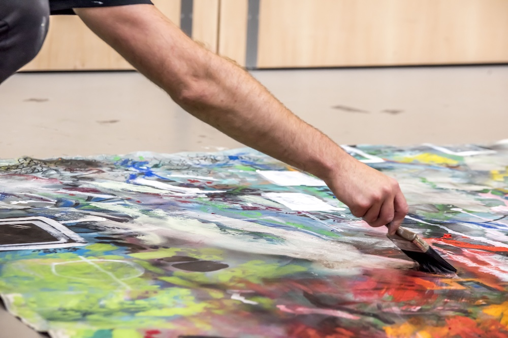 A close of a man's arm and hand painting a large abstract canvas