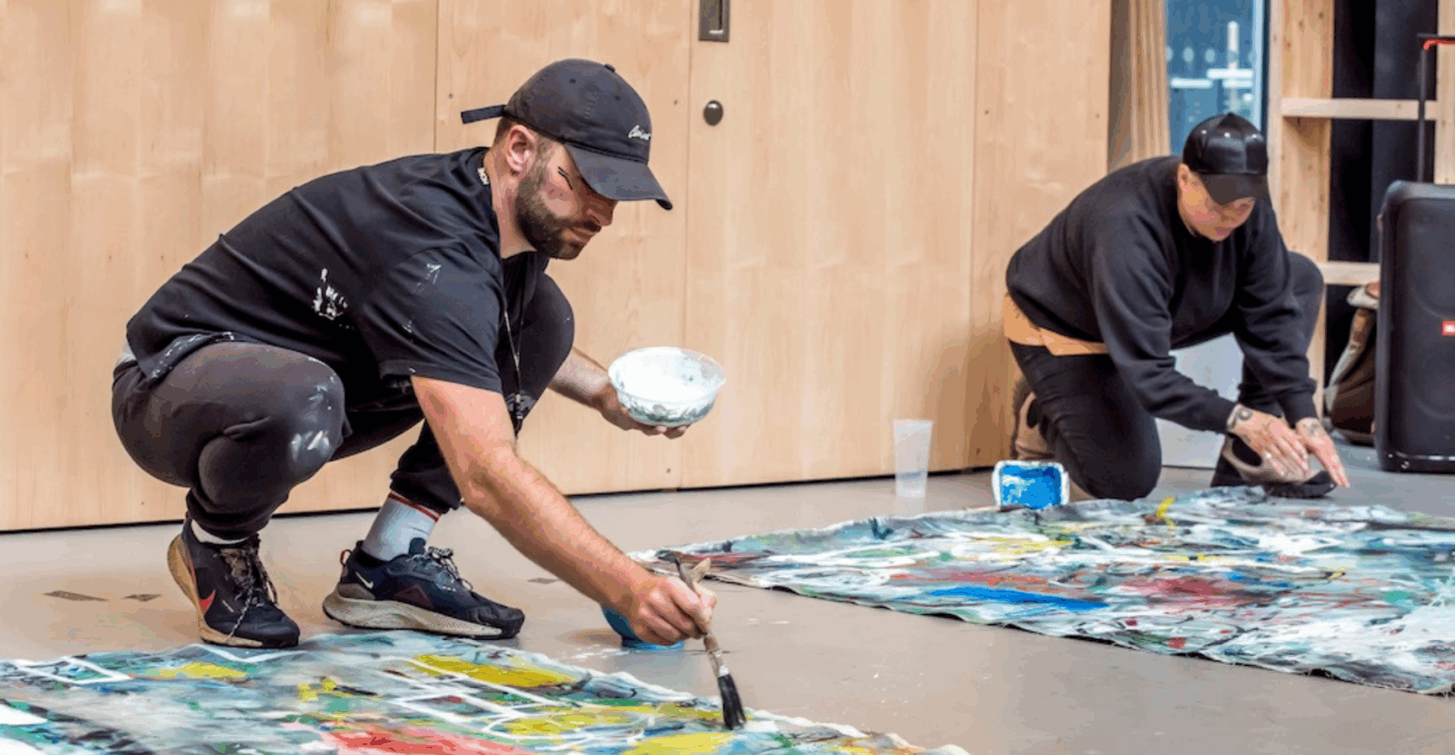Two men painting canvases on the floor as part of Artefacts of interaction