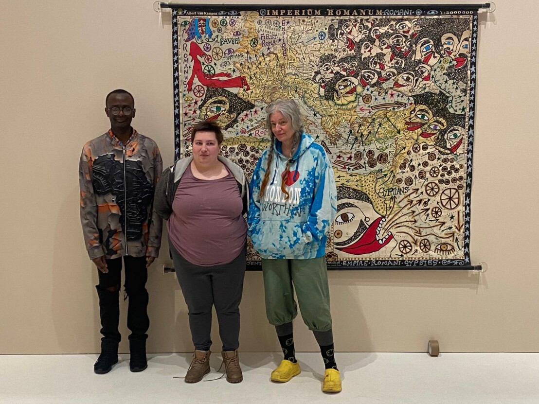 Artist Delaine Le Bas stands with two Venture Arts artists Leslie Thompson and Sarah Lee. They are standing infront of a large piece of Delaine's artwork.
