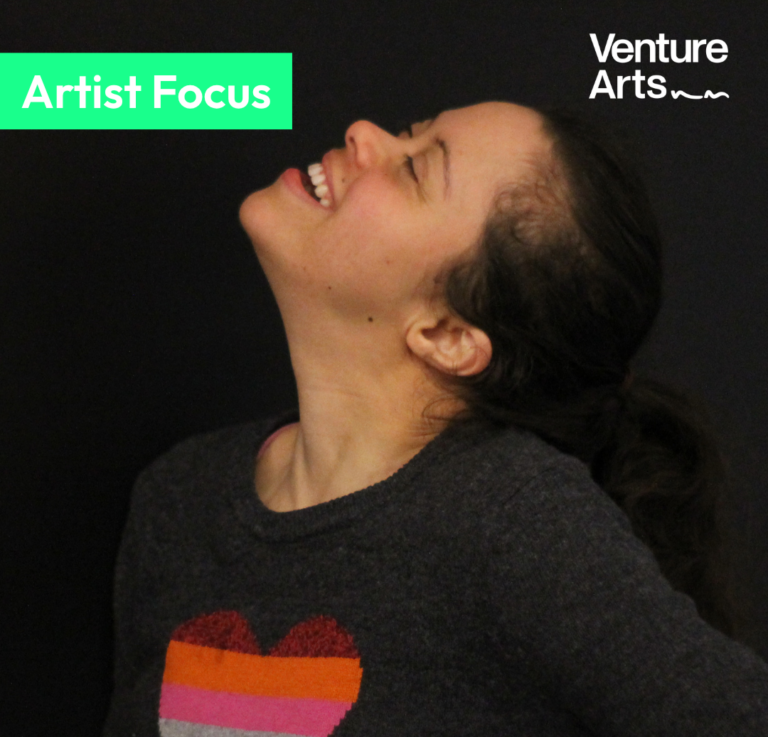 A head and shoulders picture of Artist Rhea Holmes. Rhea is turned to the side and looking up to the sky. She wears a black jumper with a rainbow coloured heart on it. The Venture Arts logo is in the top right hand corner and there is a green block on the top left hand side with the words artist focus in white. At the bottom of the picture are the words "Rhea Holmes Studio Artist".