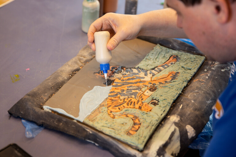 Artist, Andrew Johnstone, working in ceramics creating a flat square work with a tiger on it.